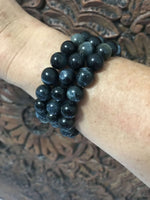 three blue tigers eye bracelets on a woman's arm against a carved indian wood board