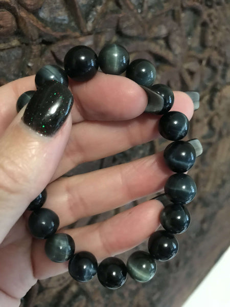 blue tigers eye crystal bracelet being held by a woman's hand with black nails against a carved indian wood board