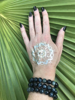 three blue tigers eye bracelets on a woman's arm with a gold tattoo black nails against a green palm leaf