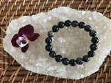 blue tigers eye crystal bracelet by a maroon orchid flower on a white apophyllite crystal on a wicker tray