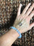 light blue chalcedony crystal bead bracelet on a woman's arm against a woven chair