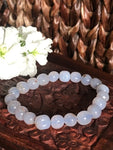 chalcedony crystal  bead bracelet laying on a wooden carved box next to white stock flowers and against a woven chair