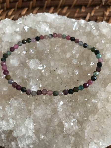 faceted mixed tourmaline crystal bracelet - pink brown purpole gray and blue beads on a white apophyllite crystal on a wicker tray