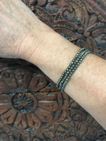 three gold pyrite faceted crystal stretch bracelets on a woman's arm against a dark indian carved piece of wood