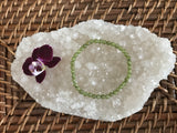 6 mm bead light green peridot crystal stretch bracelet by a maroon orchid flower on a white apophyllite crystal on a wicker tray