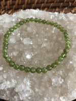 6 mm bead light green peridot crystal stretch bracelet on a white apophyllite crystal on a wicker tray