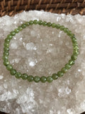 6 mm bead light green peridot crystal stretch bracelet on a white apophyllite crystal on a wicker tray