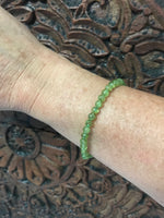 6 mm bead light green peridot crystal stretch bracelet on a woman's arm against an indian carved wooden board