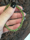6 mm bead light green peridot crystal stretch bracelet being held by a woman's hand against a dark carved indian board