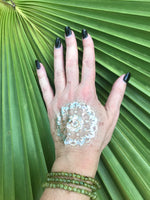 three 6 mm bead light green peridot crystal stretch bracelets on a woman's arm with a gold press on tattoo on her hand with black nails against a green palm leaf