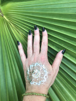 6 mm bead light green peridot crystal stretch bracelet on a woman's arm with a gold press on tattoo with black nails against a green palm leaf