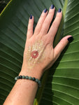 a green jade crystal bead bracelet on a woman's wrist with a gold tattoo and purple fingernails on a green leaf