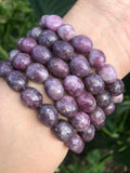 five light purple lepidolite crystal bracelets on a woman's arm against greenery