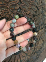 mixed tourmaline crystal bead bracelet - black purple yellow white gray green beads - held by woman's hand against wooden carved board