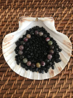 a large bead mixed tourmaline crystal bracelet set in black rocks on a shell on a wicker basket