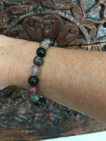 a mixed tourmaline crystal bracelet with black purple green gray beads on a woman's arm against a carved indian wood board