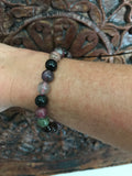 a mixed tourmaline crystal bracelet with black purple green gray beads on a woman's arm against a carved indian wood board
