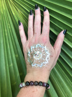 a large bead mixed tourmaline crystal bracelet - purple, green, gray, white beads on a woman's arm with a gold tattoo black nails against a green palm leaf