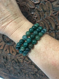 three moss agate crystal bead bracelets on a woman's arm against a dark carved indian wooden board
