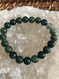 a dark green and lighter hues of green moss agate bead bracelet on a white apophyllite crystal on a wicker tray