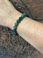 a green moss agate crystal bracelet on a woman's arm on a wooden carved indian board
