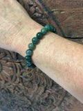 a green moss agate crystal bracelet on a woman's arm on a wooden carved indian board