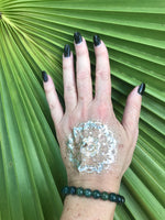 a dark green moss agate bead crystal bracelet on a woman's arm with a gold tattoo black nails against a green palm leaf