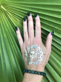 a dark green moss agate bead crystal bracelet on a woman's arm with a gold tattoo black nails against a green palm leaf