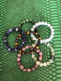 sodalite, ruby zoisite, aquamarine, tiger's eye, prehnite, lepidolite crystal stretch bracelets on a green snakeskin print tray