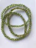 three 6 mm bead green peridot crystal stretch bracelets against a white background