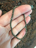 gold pyrite faceted crystal stretch bracelet being held by a woman against a carved dark wood board