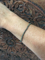 pyrite crystal stretch bracelet on a woman's arm against a dark indian carved wood board