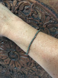 pyrite crystal stretch bracelet on a woman's arm against a dark indian carved wood board