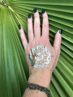 three gold pyrite faceted crystal stretch bracelet on a woman's arm with gold tattoo against a green palm leaf