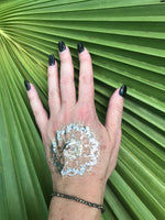 pyrite crystal stretch bracelet on a woman's arm with a gold press on tattoo with black nails against a green palm leaf