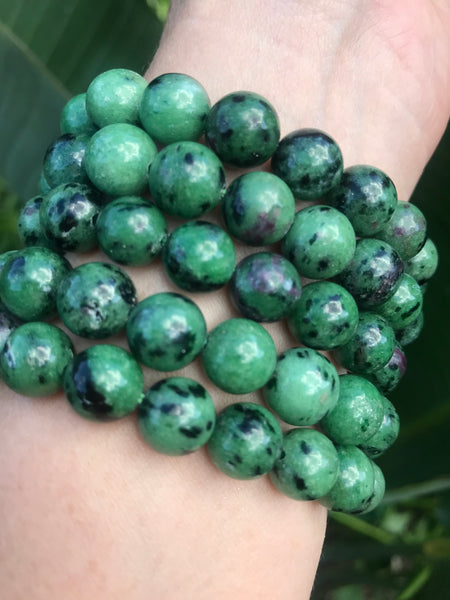 three ruby zoisite crystal stretch bracelets on a woman's arm against greenery