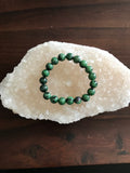 green and purple ruby zoisite crystal bracelet on a white apophyllite crystal on a wood table