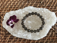 brown smoky quartz crystal stretch bracelet faceted bead laying on a white apophyllite crystal near a maroon orchid flower on top of a wicker tray