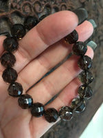 brown faceted bead smoky quartz crystal stretch bracelet being held up by a woman in front of an indian carved dark wood board