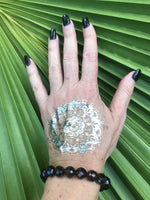 brown faceted bead smoky quartz crystal stretch bracelet on a woman's arm where her hand is in front of a green palm leaf