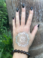 brown faceted bead smoky quartz crystal stretch bracelet on a woman's hand that is placed on top of a palm tree trunk