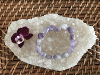 a light purple white gray tumbled bead amethyst crystal bracelet near a maroon orchid flower on a white apophyllite crystal on a wicker tray