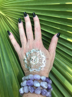three light purple white and gray tumbled bead amethyst crystal bracelets on a woman's arm with a gold tattoo with black nails on a green leaf