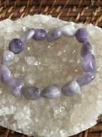 a light purple white gray tumbled bead amethyst crystal bracelet on a white apophyllite crystal on a wicker tray