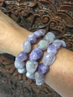 three light purple gray and white tumbled amethyst stretch bracelets on a woman's arm against an indian carved board