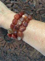 three orange tumbled carnelian crystal stretch bracelets on a woman's arm against a carved indian wood board