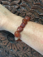 orange tumbled carnelian crystal stretch bracelet on a woman's arm against a carved indian wood board