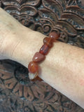 orange tumbled carnelian crystal stretch bracelet on a woman's arm against a carved indian wood board