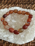 an orange tumbled carnelian crystal bracelet on white apophylite crystal on a wicker tray