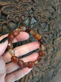 an orange tumbled carnelian crystal  bracelet being held by a woman's hand against a dark wooden carved indian board